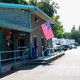 Shows the RV Park office/building with an American flag and a line of RVs parked along a paved drive — an on-site facility image consistent with the RV Park page background.