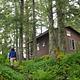 Someone walking up to a brown cabin with lots of trees around