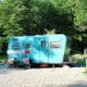 Teal vintage travel trailer on a gravel site among trees — shows RV pitch/site setup and atmosphere (amenities gallery image on the property site).