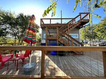 Alternate bright-angle view of the same deck/patio structure with chairs, umbrella and stair access — useful to show outdoor recreation and seating areas from the park homepage (The Buzz RV Park, https://www.thebuzzrv.com/).