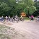 Shot of a bike parade with small cabins visible in the background and campsite road — demonstrates campground layout, activities and cabin accommodations.