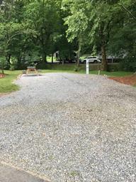Campsite with gravel pad, utility hookup and an RV visible in background — useful to show actual RV-scale site and on-site vehicle context (from Sites page).