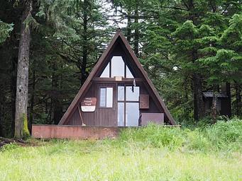 Brown A-Frame Cabin with steps leading up to it and trees behind and beside it. Berg Bay Cabin