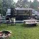 Clear view of an RV campsite with a trailer, picnic table, fire ring and paved pad—useful to show site setup and amenities (source: site gallery).