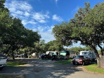 A row of rvs are parked in a parking lot surrounded by trees.