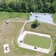 Wide stitched/drone collage from the property homepage showing multiple panoramic views of the pond, picnic area and surrounding campsites — useful overview of site layout and amenities.