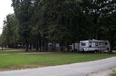 Photo of RVs and campsites among trees with picnic tables and gravel road — shows typical site/RV pitch setup; sourced from About page content about the campground.