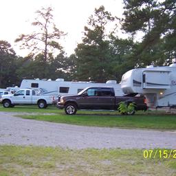 Row of RVs and pull-through sites with trucks visible on gravel pads and tree-lined background — clearly shows typical RV camping spaces at this KOA (from 'Ways to Stay' imagery).