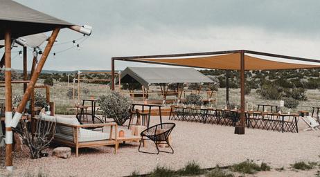 Wide view of an outdoor seating/communal area with shade structure, tables and lounge seating — useful for showing on-site guest facilities and gathering space (photo is on the property website).