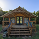 Front view of a larger wooden cabin with porch and steps — shows another lodging/facility type and outdoor seating area promoted on the site.
