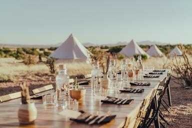Foreground dining table set for guests with bell tents visible in the background — shows on-site dining/experience offerings and relationship to the campsite area (hosted on property pages).