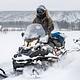 A snowmobiler rides past a log cabin 
