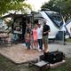 Family posed in front of a large RV on a landscaped site with brick patio and fire ring — highlights a typical full-hookup RV campsite and social aspect of the campground.