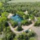 Aerial/drone overview showing the campground layout, pond with fountain, paths, and multiple yurts/wagons — good high-level property view (file shown on The Stays page as a drone image).