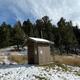 Concrete outhouse surrounded by green trees and snow