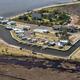 Aerial photo of a waterfront RV park with boat canal, docks, cottages, swimming pool, and parked RVs beside marshland.
