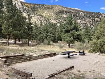 campsite with picnic table and fire pit with blue sky and mountains in background.