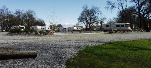 Panoramic header image showing multiple RVs on gravel pads beside water and trees — good wide view of the park’s campsite area (site header background).