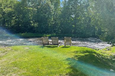 Riverside seating area with three chairs on the riverbank — highlights waterfront scenery and guest relaxation spots (gallery image G8).