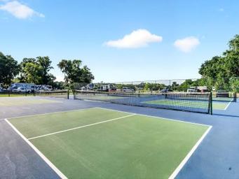 Outdoor photo of the tennis/pickleball courts with RV sites visible in the background — highlights recreational facilities on the property; included on the amenities page.