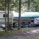 RV parked at a shaded campsite with awning, chairs and campsite setup — directly illustrates RV pitching and wooded campsite environment on the property.