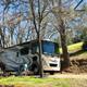 RV parked at a site with hookups and picnic setup among trees and grassy slope — good representation of RV accommodations on the grounds.