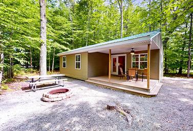 Clear exterior photo of a cottage on gravel pad with porch, picnic table and fire ring — good representation of on‑site cottages referenced on the property’s accommodation pages.