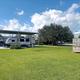 Ground-level view of covered RV pads and adjacent lawn with the park sign visible — useful for showing RV pitch style and on-site amenities (homepage).