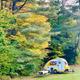 Clear on-site photo of a small teardrop trailer on a grassy campsite with picnic table and surrounding trees — appears on the campground gallery page (IMG_5812), showing an authentic campsite view of the property.