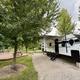 Exterior view of a rental camper on a gravel pad with deck, picnic table and shaded trees — useful depiction of RV/camper sites from the Rental Camper page.