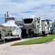A fifth wheel and a covered boat on its trailer parked side by side at one site