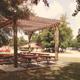 Covered picnic pergola and picnic tables with campground grounds and buildings visible in background — clear on-site amenity photo from the park homepage (https://rainbowsend.escapeesrvparks.com/).