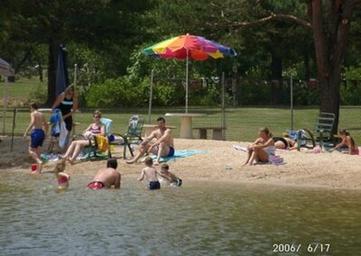 Beach area on the lake with people, umbrella and swimming shore — demonstrates waterfront/beach amenities (from the Camping photo gallery).