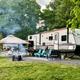 Active RV site with a travel trailer, canopy, chairs and firepit area — clearly depicts the campground’s RV camping setup and guest amenities.