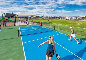 Daytime image of on-site pickleball courts with resort grounds and RVs visible beyond — demonstrates recreational facilities located on the campground property (matches ‘amenities’ page content).