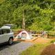 Tent campsite with vehicle parked nearby, tent pad, picnic table and wooded backdrop — depicts tent camping sites on the property (from the campground’s site 'ways to stay' photos).