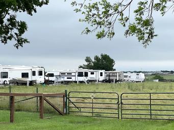 Ground-level view of multiple parked RVs behind a gate and pasture — good for demonstrating campsite density and rural setting (from About Us page).