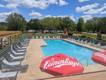 Elevated view of the heated outdoor pool with lounge chairs and part of the campground beyond — shows pool facility and nearby RV/campsite area.