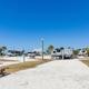Gravel RV park with multiple campers, picnic tables, palm trees, and clear blue sky. No people visible.
