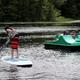 Waterfront activity shot showing paddleboard and pedal boat on a small lake/pond — matches the campground's lake recreation described on the property page and appears to be taken on-site (used as the page's social/hero media).