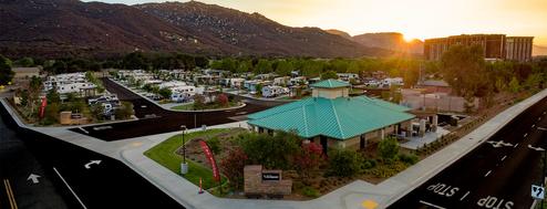 Panoramic hero-style photo at sunset showing the resort clubhouse, RV sites and nearby hotel with hills in background — good wide context and atmosphere.