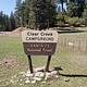 A campground sign with spruce trees and clear blue skies in the background.