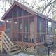 Close exterior view of a standalone cabin with screened porch and surrounding trees — good alternate cabin detail and visitor view.
