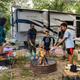 Clear photo of an RV site with a family around a fire ring and an RV in the background — demonstrates typical RV pitch layout and amenities (fire ring, chairs), matching the site’s ‘RV sites’ gallery context.