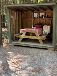 Covered picnic shelter with a picnic table and gear—depicts on-site campsite amenities and dining/food-preparation area; appears in the site’s gallery pages.