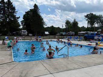 Main pool photograph showing the pool, deck and RVs/campsites in the background — clearly a core amenity of the campground from the official site.