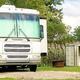 A motorhome parked near a shed and golf cart in a grassy area.