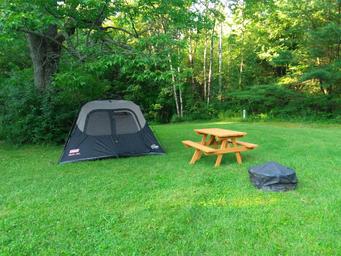 Open grassy tent campsite with picnic table and fire pit — clear depiction of primitive tent camping spots available on the grounds (tent camping image on site).