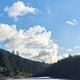 Blue lake with sand and grass covered shore in foreground and conifer forest in background.
