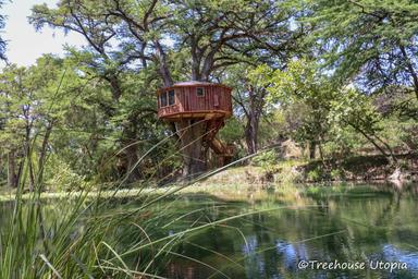 Small round treehouse by a pond with reflected water and natural vegetation — shows on-site scenery and setting, useful for highlighting grounds and water feature (homepage imagery).